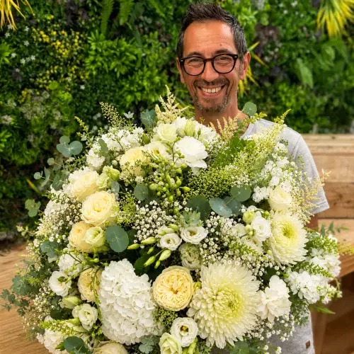 Dominique, fleuriste, avec un grand bouquet blanc dans la boutique Au Delà des Fleurs